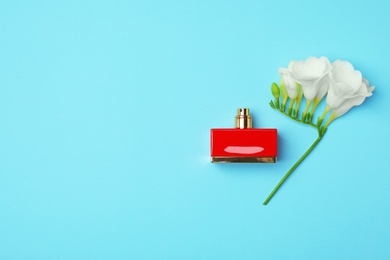 Photo of Bottle of perfume and flower on color background, top view