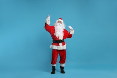 Photo of Merry Christmas. Santa Claus pointing at something on light blue background