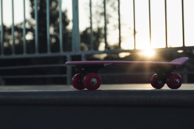 Modern pink skateboard with red wheels on top of ramp outdoors at sunset