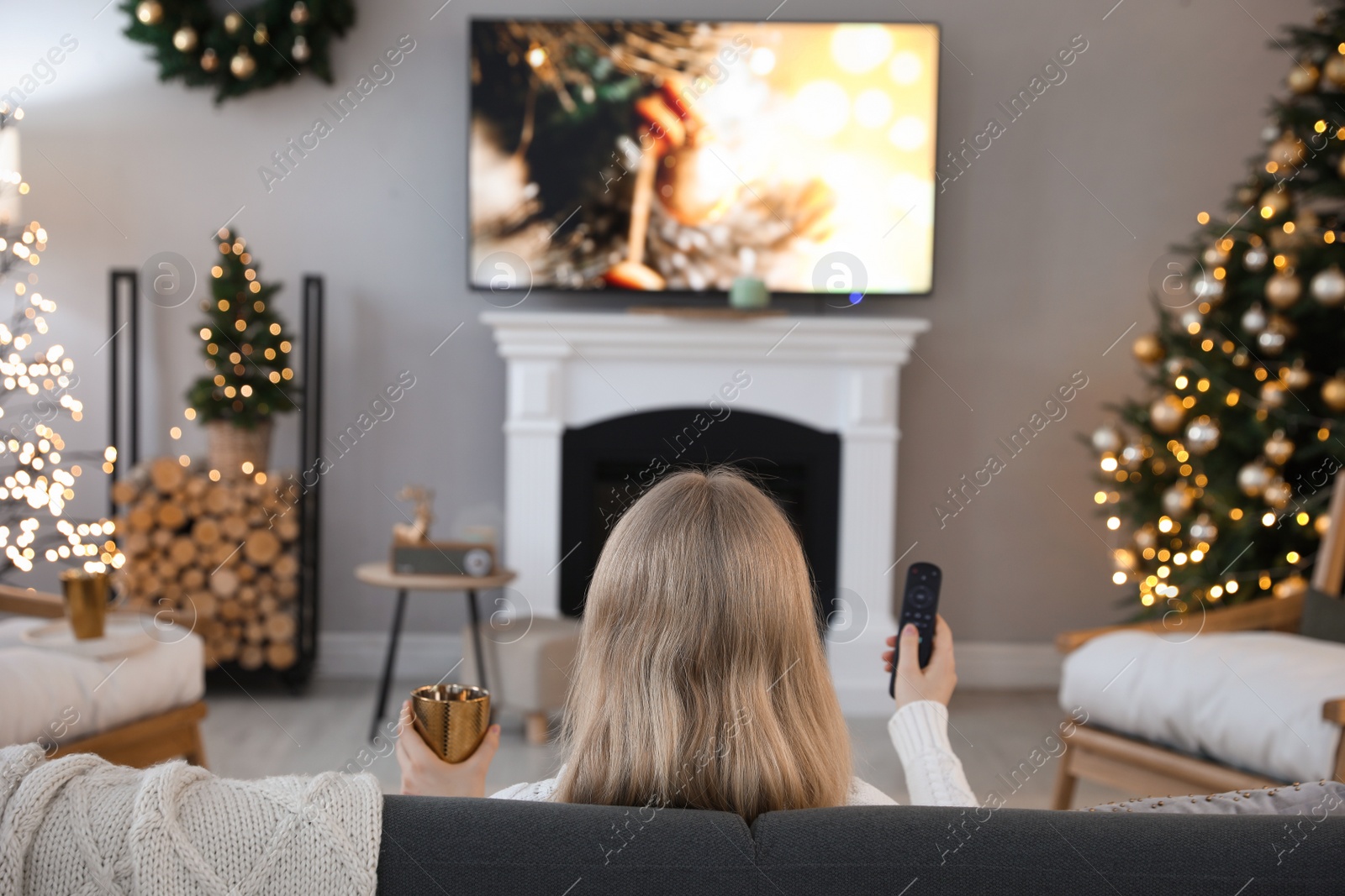 Photo of Woman on sofa watching TV in room decorated for Christmas, back view