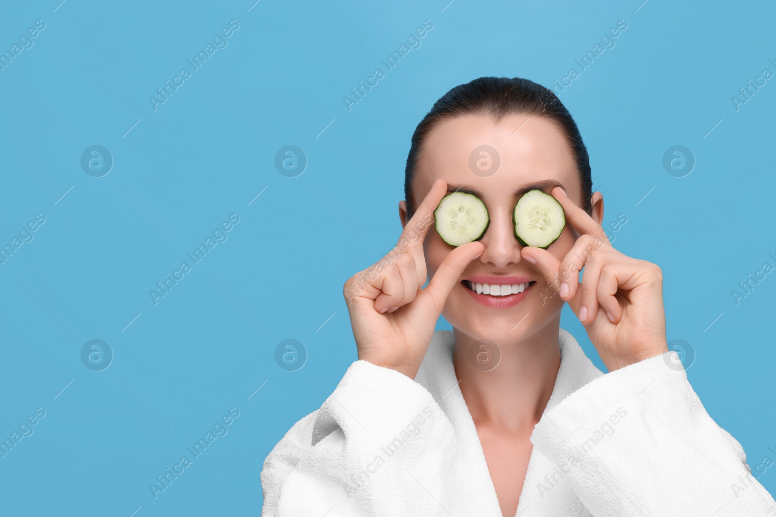 Photo of Beautiful woman covering eyes with pieces of cucumber on light blue background, space for text