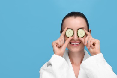 Photo of Beautiful woman covering eyes with pieces of cucumber on light blue background, space for text