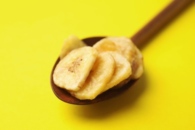 Wooden spoon with banana slices on color background, closeup. Dried fruit as healthy snack