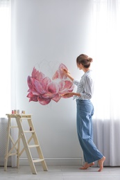 Photo of Decorator painting flower on white wall in room. Interior design