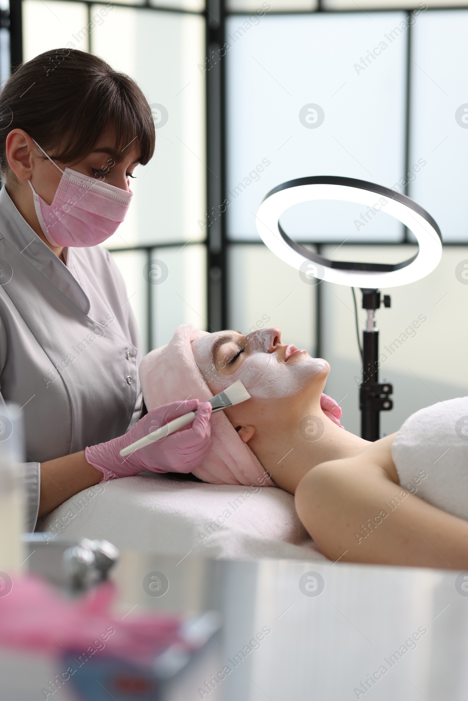 Photo of Cosmetologist applying mask on woman's face in clinic