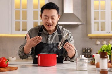 Photo of Man with pot smelling dish after cooking at countertop in kitchen