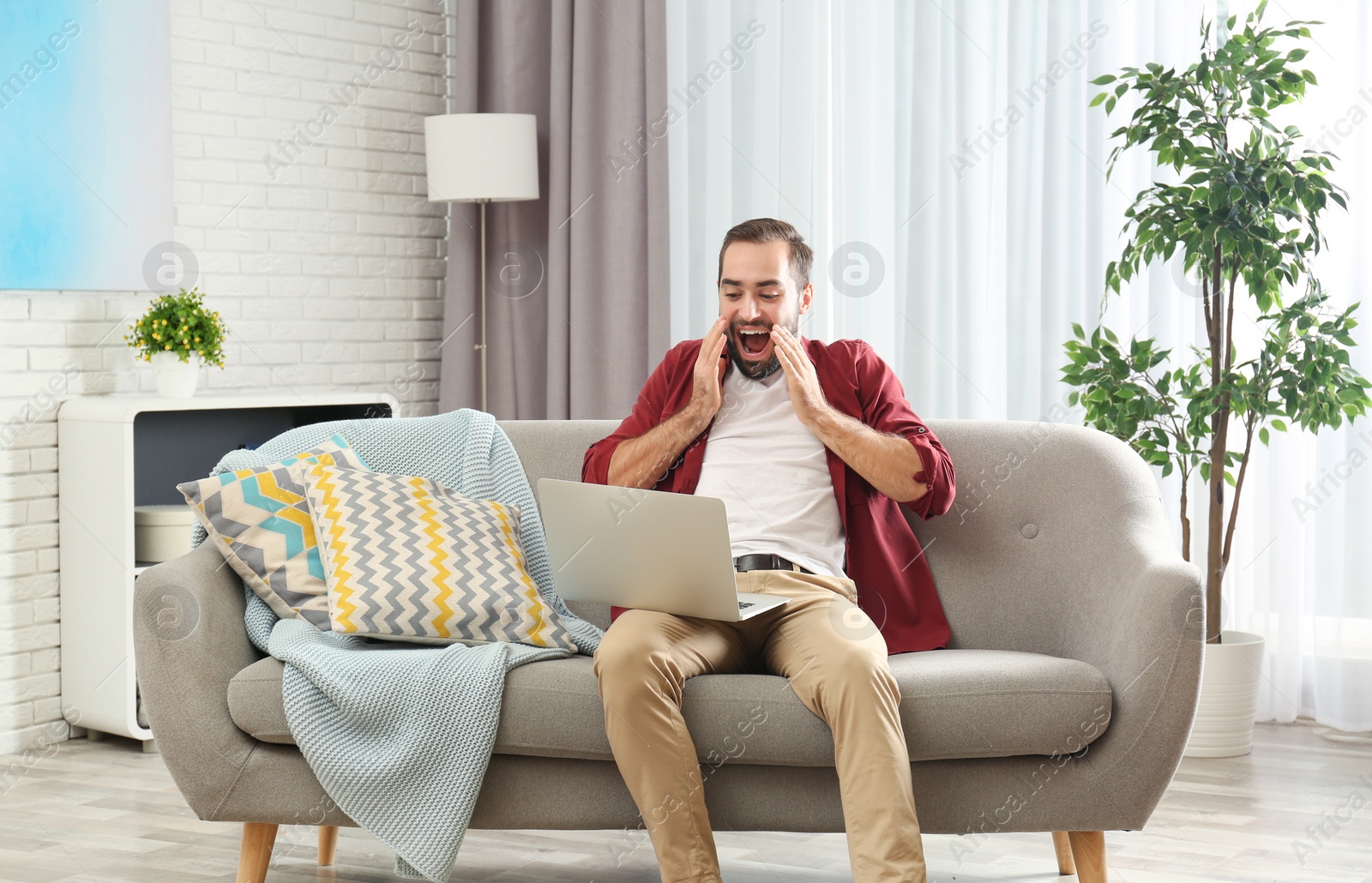 Photo of Emotional young man with laptop celebrating victory on sofa at home