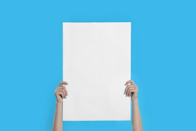 Photo of Woman holding blank poster on blue background, closeup