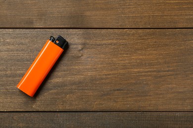 Photo of Orange plastic cigarette lighter on wooden table, top view. Space for text
