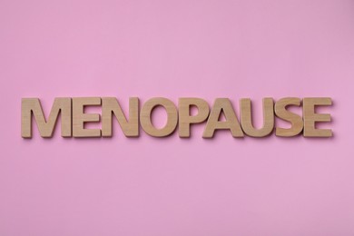 Photo of Word Menopause made of wooden letters on pink background, flat lay