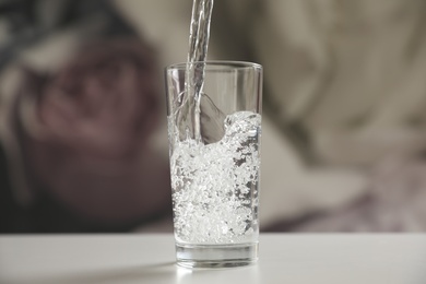 Photo of Pouring water into glass on table against blurred background