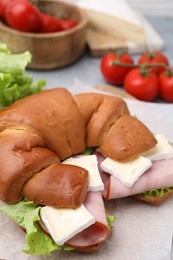 Photo of Tasty crescent roll with brie, ham and lettuce on grey table, closeup