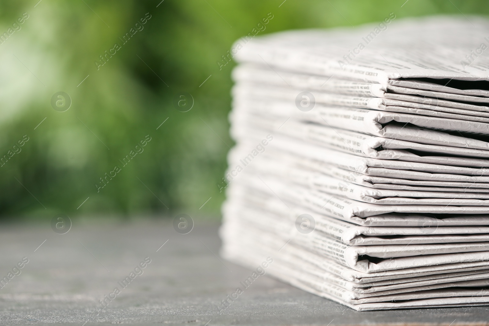 Photo of Stack of newspapers on grey table against blurred green background, space for text. Journalist's work