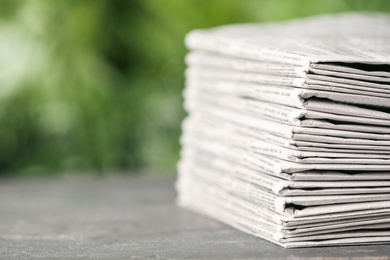 Stack of newspapers on grey table against blurred green background, space for text. Journalist's work