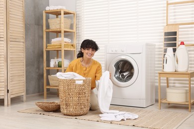 Happy woman with laundry near washing machine indoors