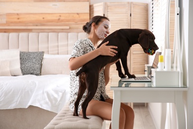 Young woman getting distracted by her dog while working with laptop in home office
