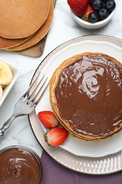 Photo of Tasty pancakes with chocolate paste, berries and fork on white marble table, flat lay