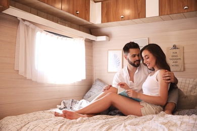 Photo of Happy young couple reading book on bed in trailer, space for text. Camping vacation