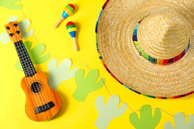 Photo of Mexican sombrero hat, maracas, ukulele and garland on yellow background, flat lay