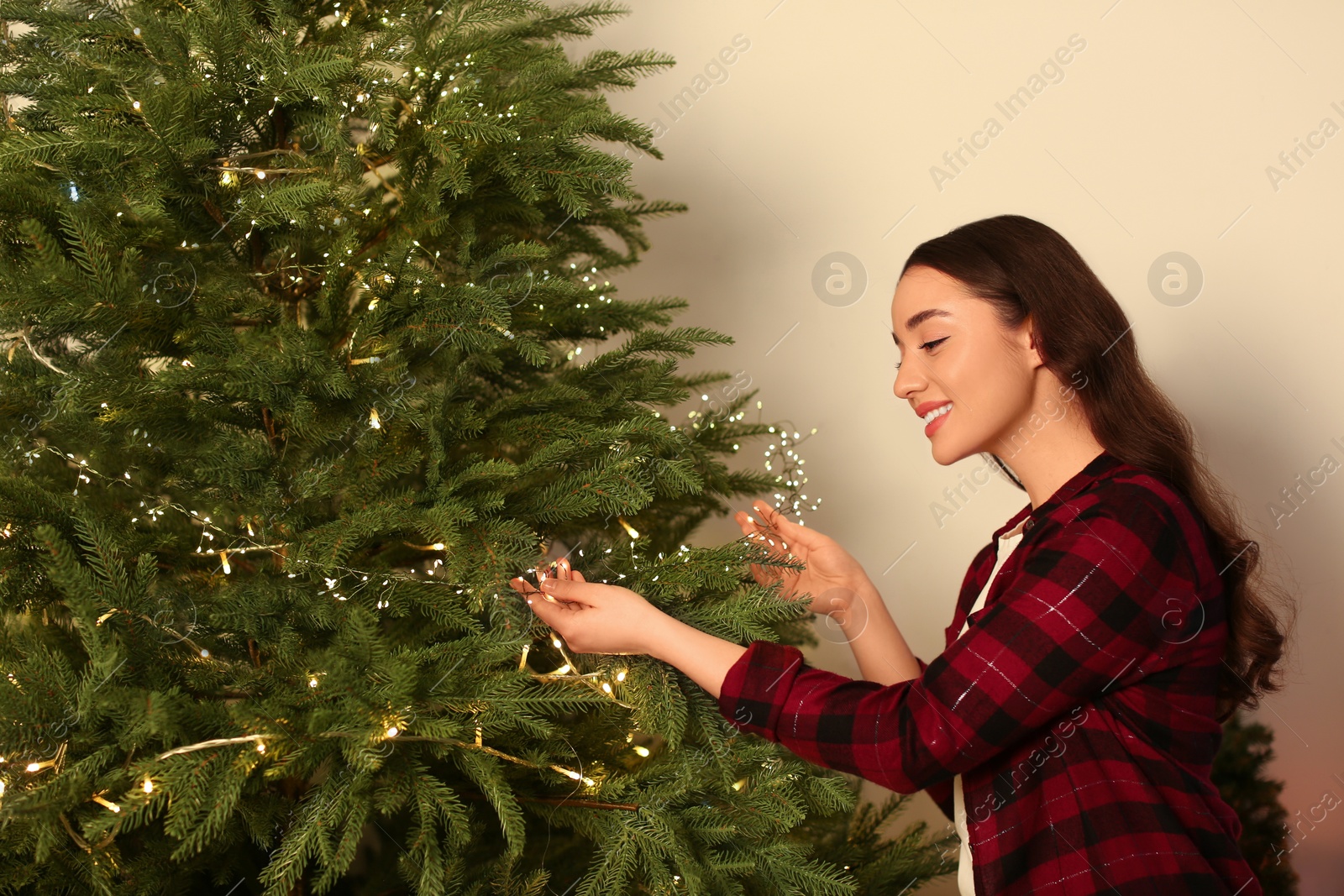 Photo of Beautiful woman near Christmas tree with golden lights indoors