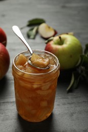 Tasty apple jam with spoon in glass jar and fresh fruits on grey table