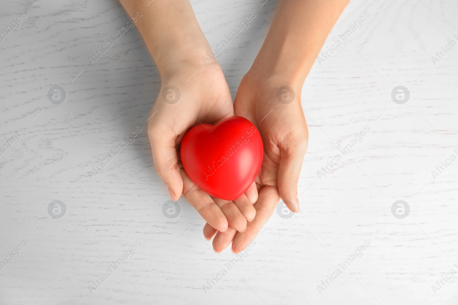 Photo of Woman holding red heart on wooden background, top view. Cardiology concept