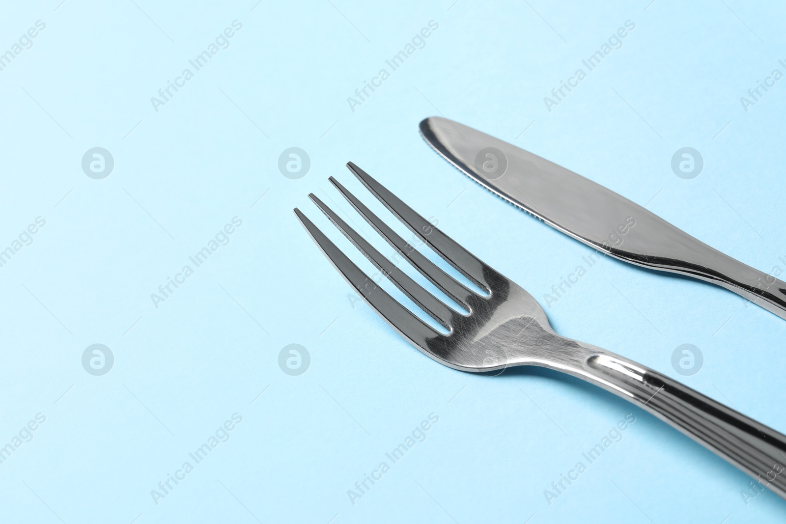 Photo of Stylish silver cutlery on light blue background, space for text