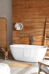 Photo of White tub and decor near wooden wall in room. Interior design