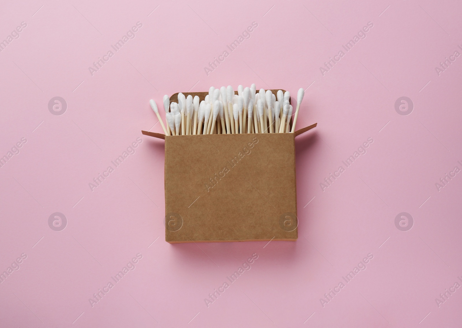 Photo of Cotton buds in cardboard box on pink background, top view