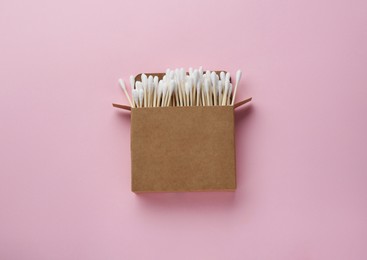 Cotton buds in cardboard box on pink background, top view