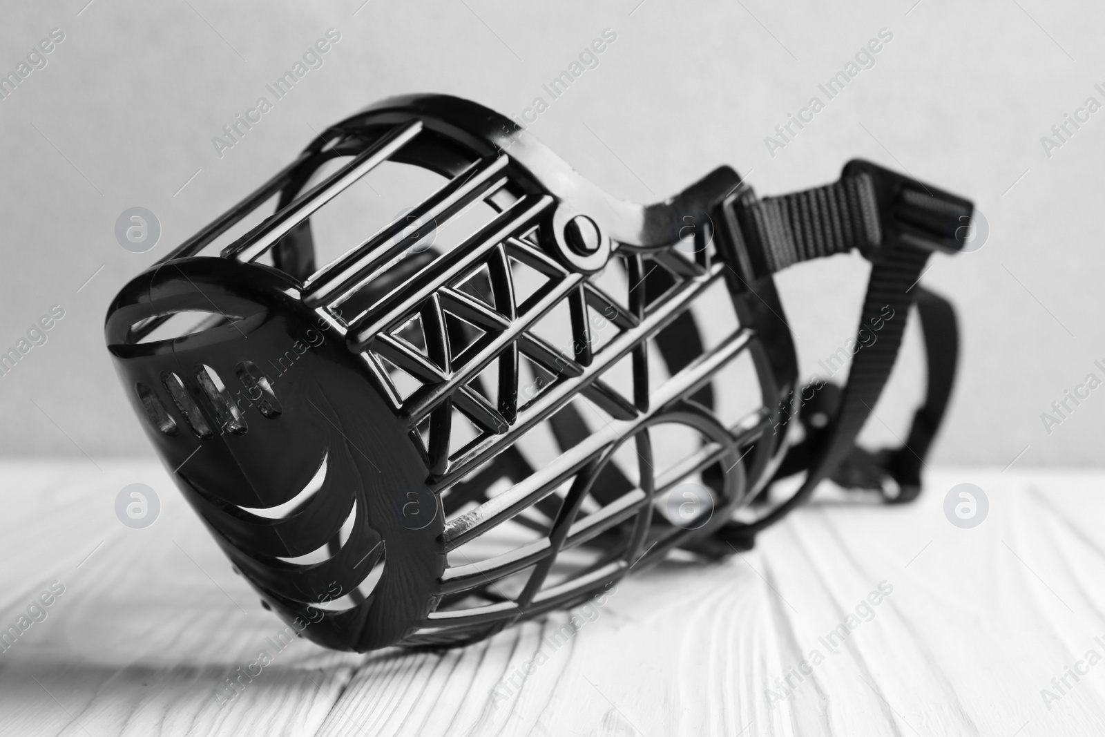 Photo of Black plastic dog muzzle on white wooden table, closeup