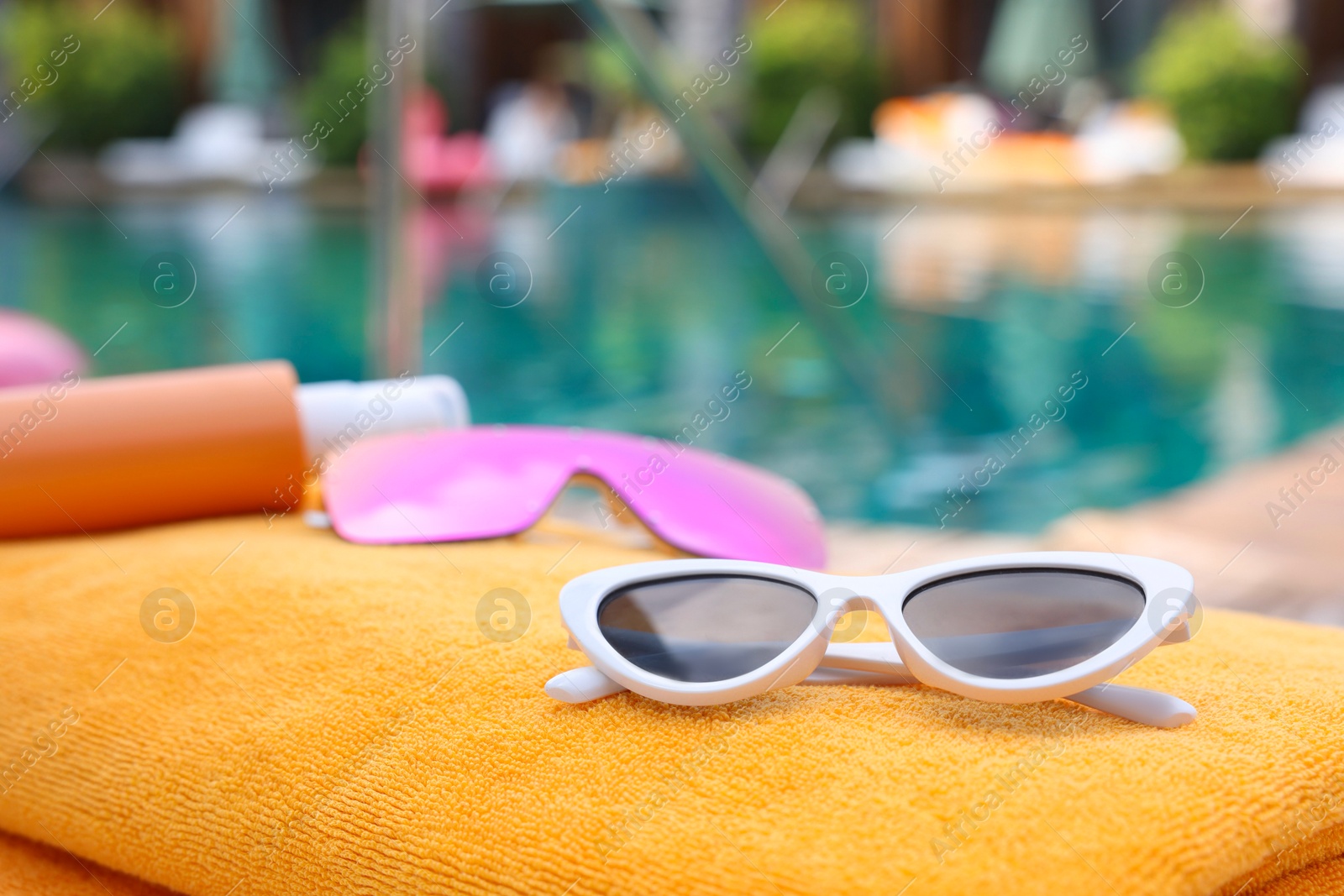 Photo of Sunglasses and sunscreen on beach towel near outdoor swimming pool at luxury resort, closeup. Space for text