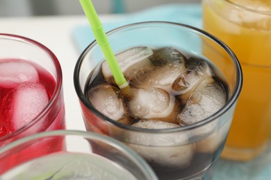 Glasses of different refreshing soda water with ice cubes and straws on white background, closeup