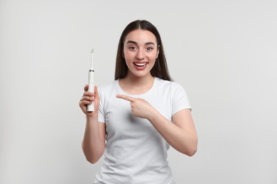 Happy young woman holding electric toothbrush on white background