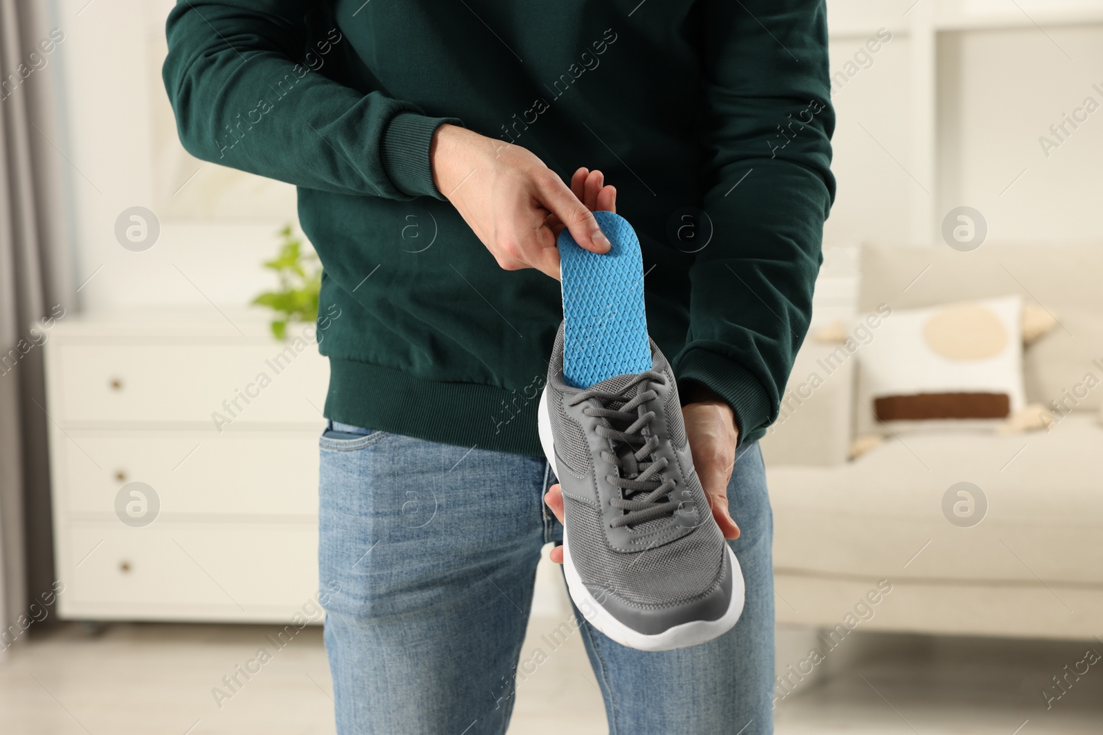 Photo of Man putting orthopedic insole into shoe indoors, closeup