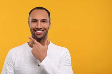 Portrait of smiling man with healthy clean teeth on orange background. Space for text