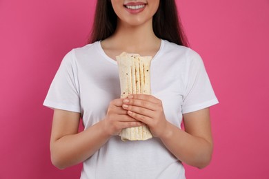 Photo of Happy young woman holding tasty shawarma on pink background, closeup