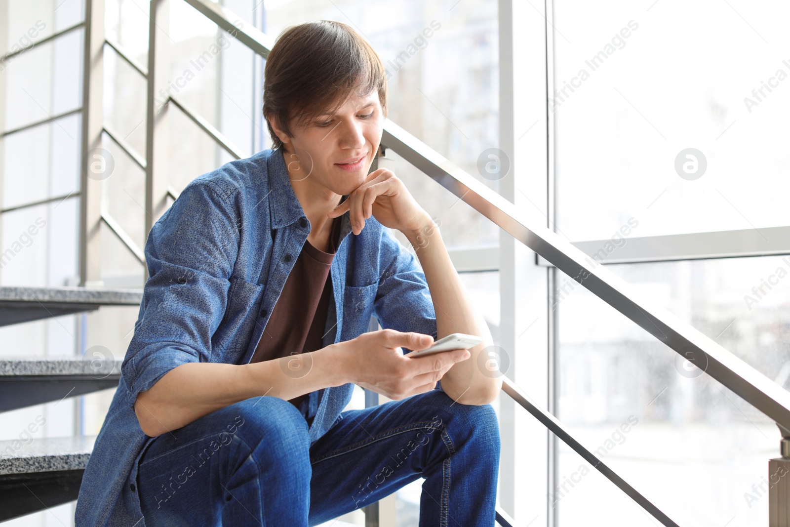 Photo of Portrait of confident young man with mobile phone on stairs