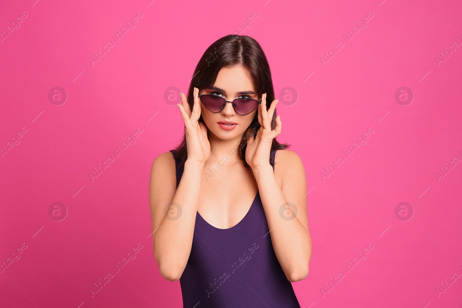 Photo of Beautiful woman in stylish swimsuit and sunglasses on pink background