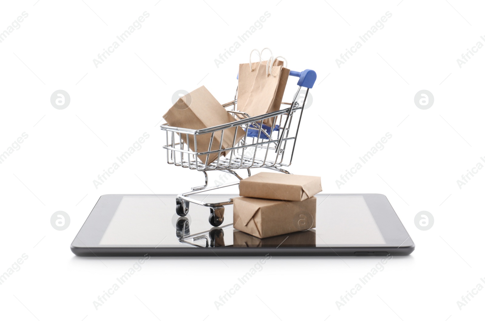 Photo of Small cart with bags and boxes on modern tablet against white background. Internet shopping