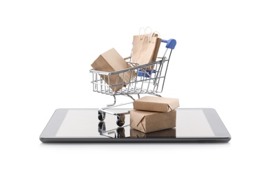 Small cart with bags and boxes on modern tablet against white background. Internet shopping