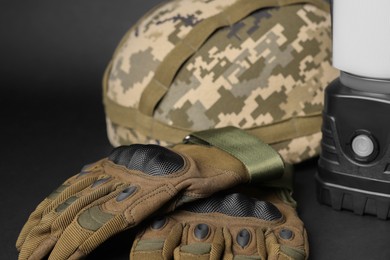 Photo of Tactical gloves, helmet and camping lantern on black background, closeup. Military training equipment