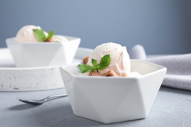 Photo of Bowl of ice cream with caramel candies and mint on light grey table