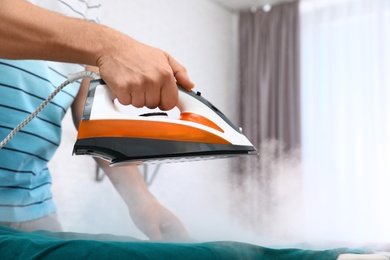 Man ironing clothes on board at home, closeup