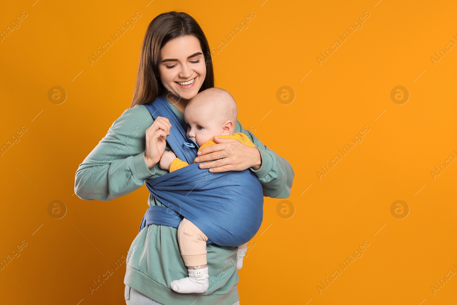 Photo of Mother holding her child in sling (baby carrier) on orange background. Space for text