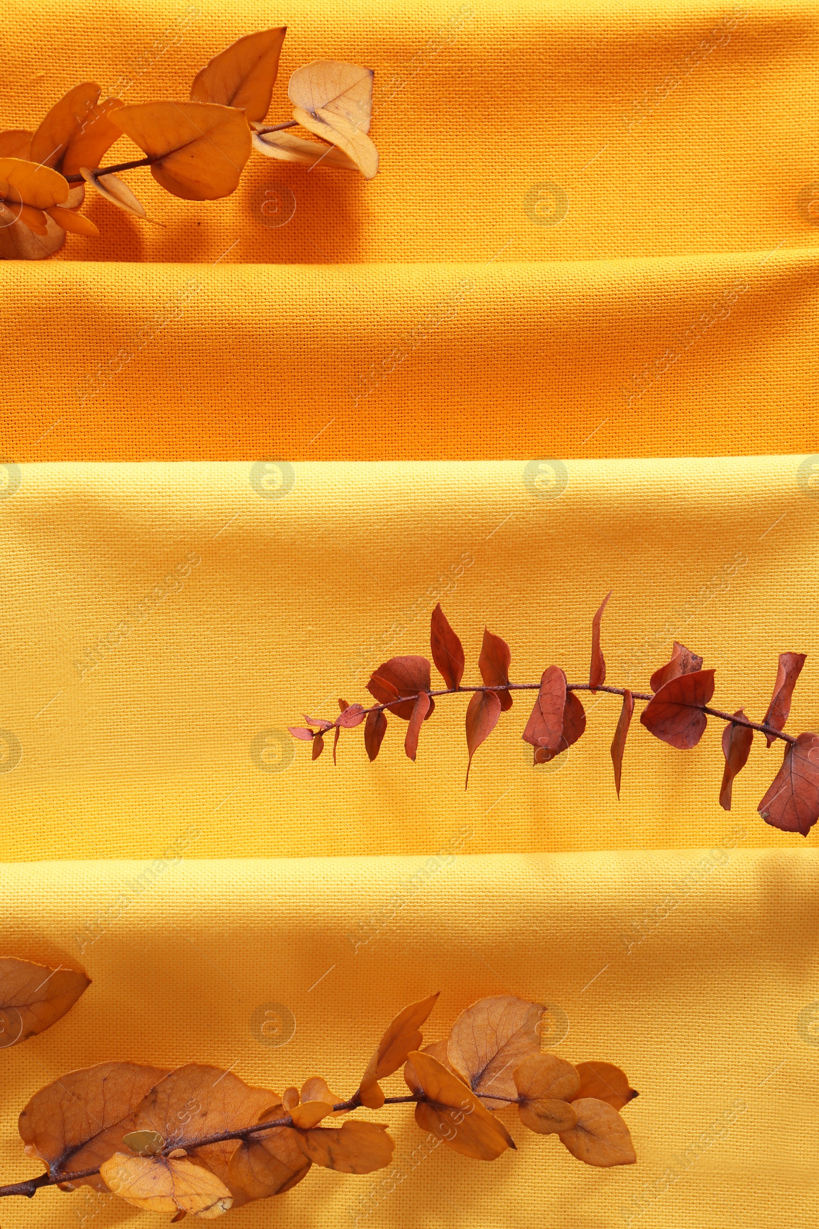 Photo of Different kitchen napkins and decorative dry leaves as background, top view