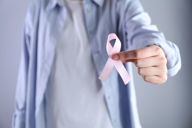 Woman with pink awareness ribbon on grey background, closeup