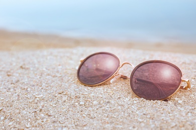 Stylish sunglasses on sandy beach near sea