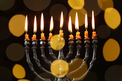 Silver menorah with burning candles against dark background and blurred festive lights. Hanukkah celebration