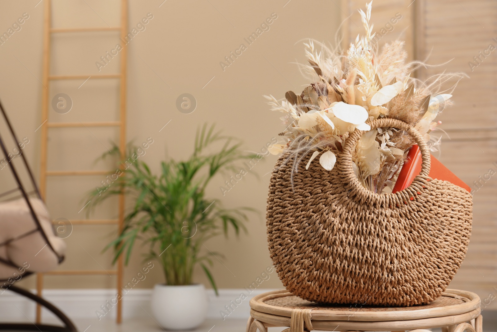 Photo of Stylish beach bag with beautiful bouquet of dried flowers and book on table indoors. Space for text